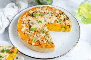 A whole savory sweet potato pie with one slice missing, topped with herbs and grated cheese, on a white plate.